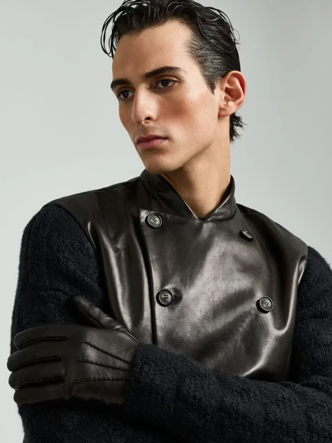 Close-up fashion shot of a man in a black leather vest and gloves against a grey backdrop, highlighting textures and sleek styling.