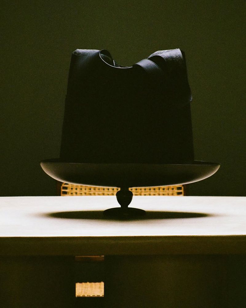 Stylized shot of an avant-garde black hat with sculptural details, resting on a dark shallow bowl, presented on a minimalist surface.