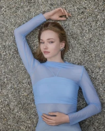 Model in sheer blue long-sleeve top lying on a textured grey gravel ground