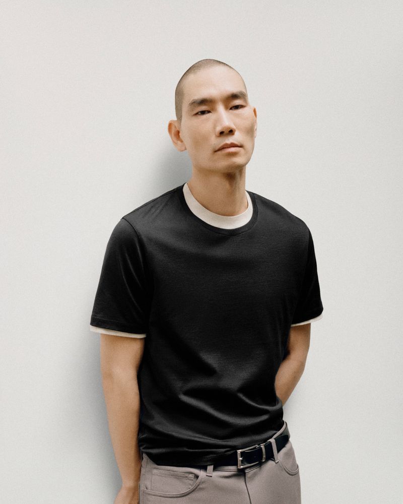 Portrait of an Asian man wearing a black t-shirt and khaki pants, posing in front of a plain white wall, simple and clean.