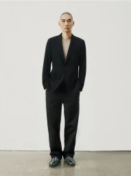 Man wearing a black suit jacket and trousers standing against a plain white studio background