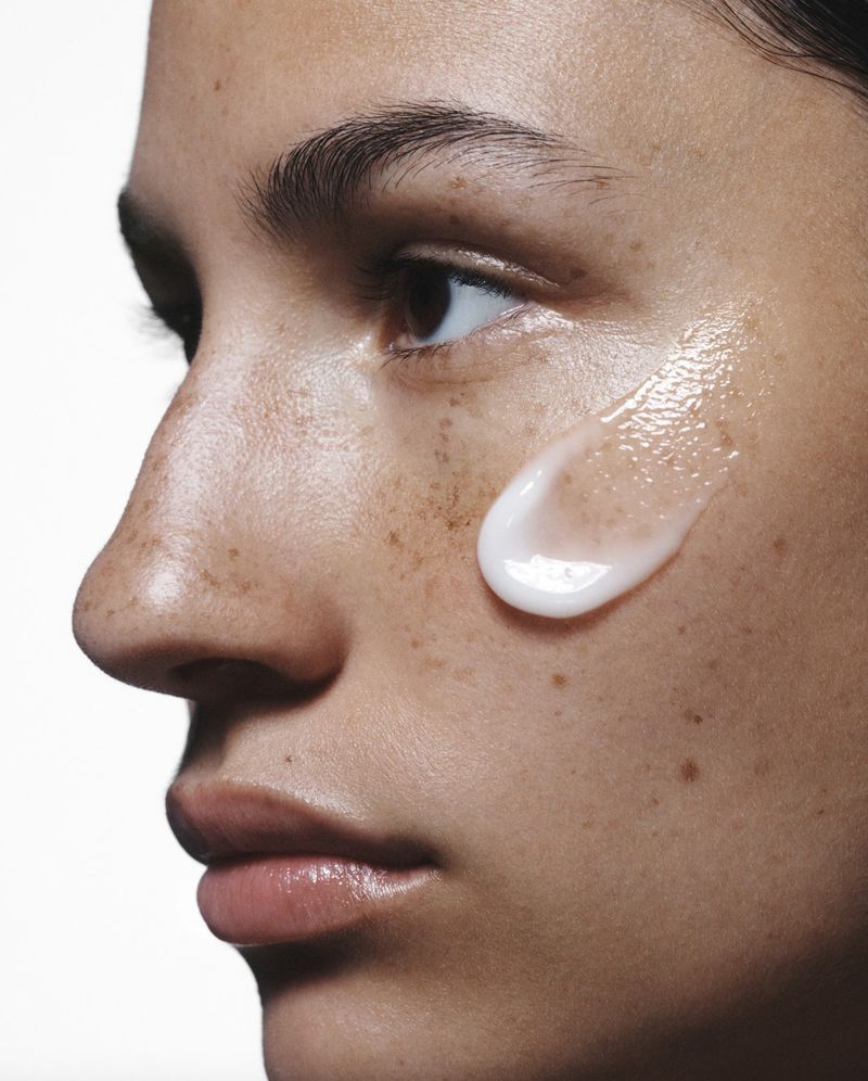 Close-up of a woman's face with a droplet of skincare product on her cheek, highlighting skincare and beauty.