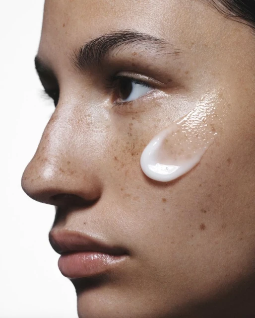 Close-up of a woman's face with a droplet of skincare product on her cheek, highlighting skincare and beauty.