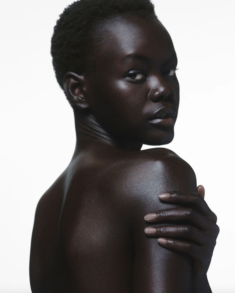 Close-up studio portrait of a dark-skinned woman with short hair. She looks over her shoulder, with her hand on her upper arm.