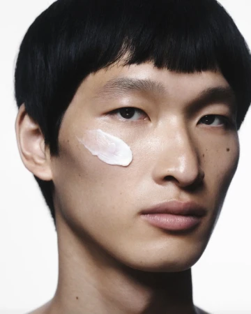 Close-up portrait of an adult man with black hair and light skin, wearing facial cream. Beauty shot with studio lighting and white background.