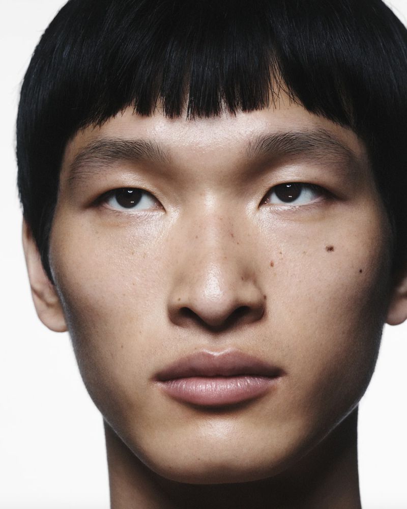 Close-up portrait of a young adult Asian man with dark hair and light skin tone, set against a plain white background.