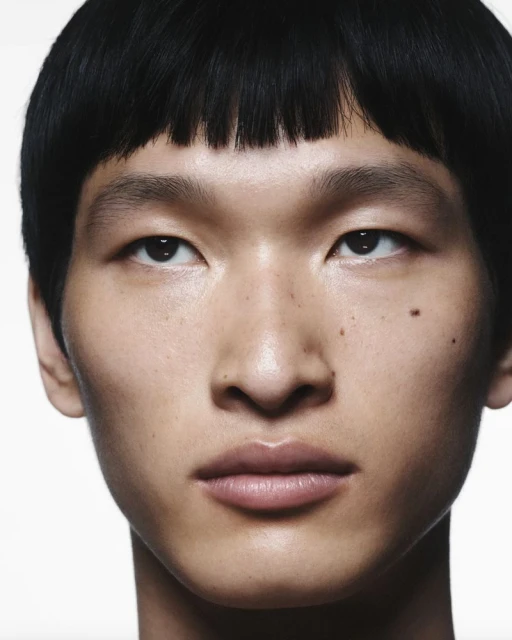 Close-up portrait of a young adult Asian man with dark hair and light skin tone, set against a plain white background.