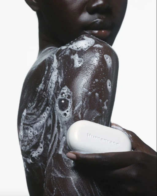 Close-up of an adult woman washing her shoulder with a white soap bar in a brightly lit studio. Focus on hygiene, skincare, and beauty.