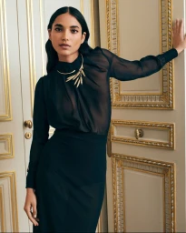 Model Amrit wearing a black sheer blouse and statement gold necklace against an ornate panelled door in a Boucheron campaign.