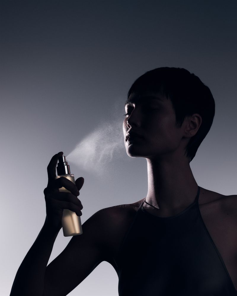 Elegant woman applying face mist. Close-up studio shot of a dark-haired model spraying her face with refreshing facial product.