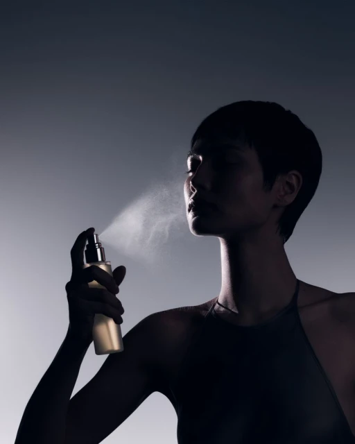 Elegant woman applying face mist. Close-up studio shot of a dark-haired model spraying her face with refreshing facial product.