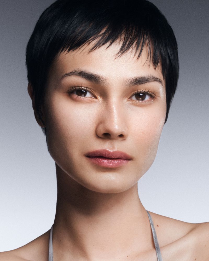 Close-up portrait of an adult woman with short, dark hair and light skin. She is wearing a silver-colored top and looking forward.