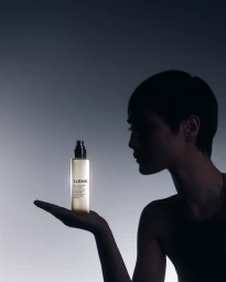 Model in silhouette holding an Elemis toner bottle in the palm of her hand against a minimalist grey gradient background