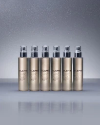 Six metallic Elemis toning mist bottles arranged in a row with a subtle reflection on a grey studio surface