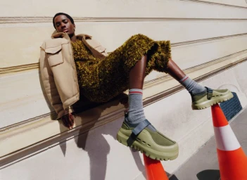 Model Alton Mason wearing green clogs resting feet on traffic cones against a classical building wall