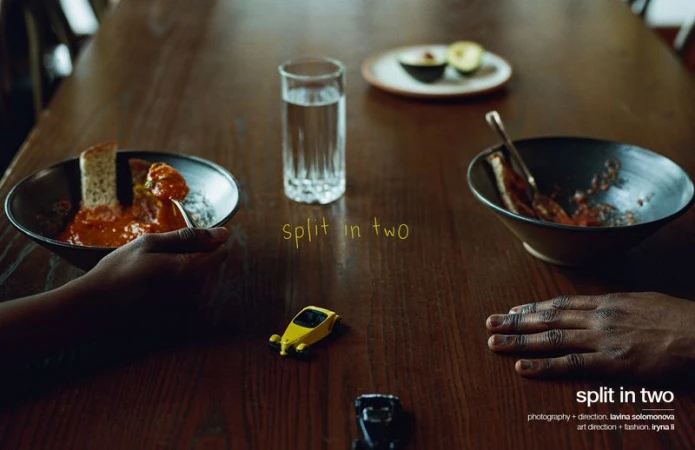 Overhead shot of a wooden table with two bowls of saucy food, a glass of water, avocado slices, and two toy cars, split between two people.