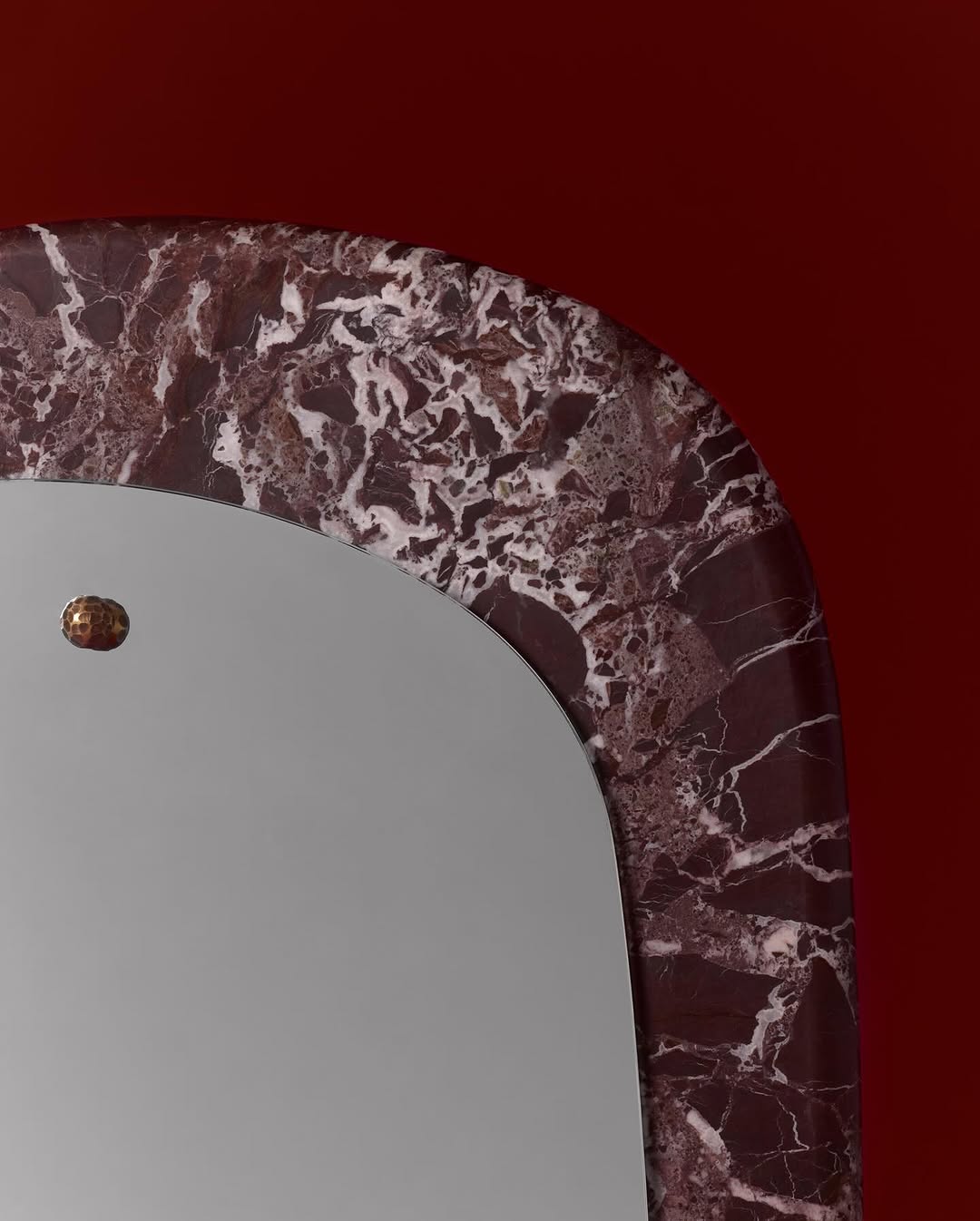 Close-up shot of an Art Deco mirror with a dark marble frame, set against a solid red background creating a warm, vintage aesthetic.