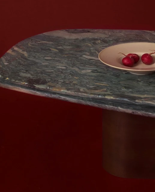 Radishes arranged on a plate placed on a marble table with a cylindrical base, all set against a dark red background.