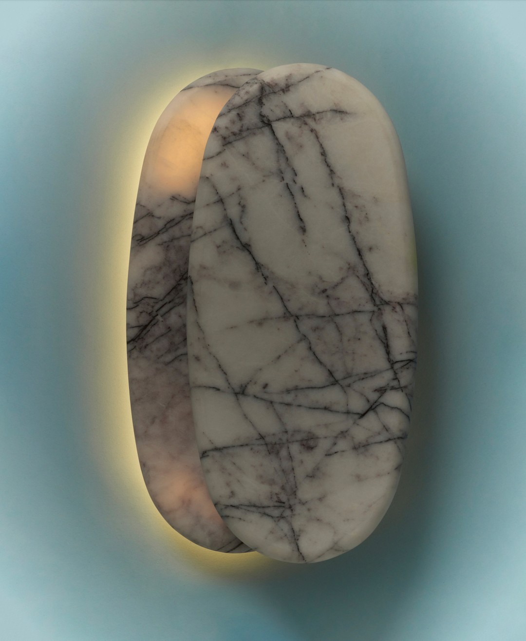 Close-up of a pair of marble wall sconces featuring a white marble finish with black veining and a soft, warm glow, mounted on a light blue wall.
