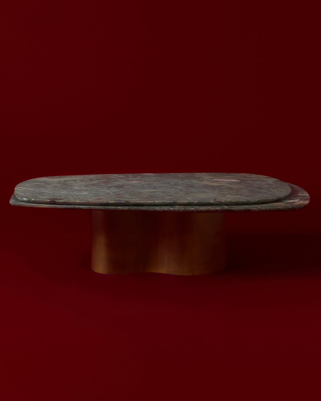 An interior design shot showing a table with a dark stone top and gold base set against a solid red studio background.