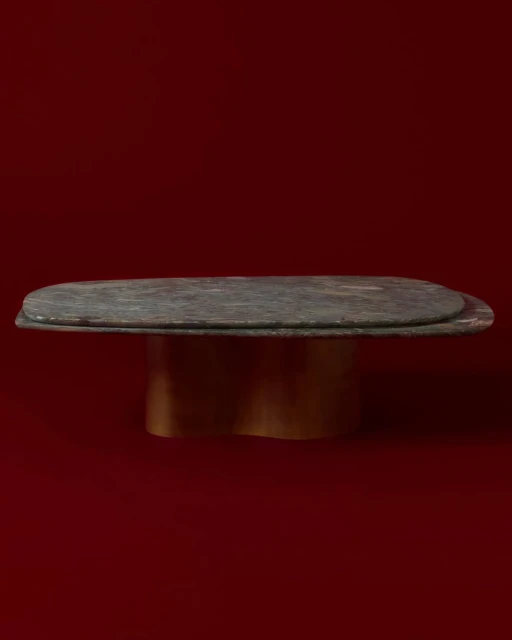 An interior design shot showing a table with a dark stone top and gold base set against a solid red studio background.