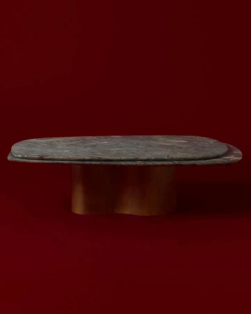 An interior design shot showing a table with a dark stone top and gold base set against a solid red studio background.