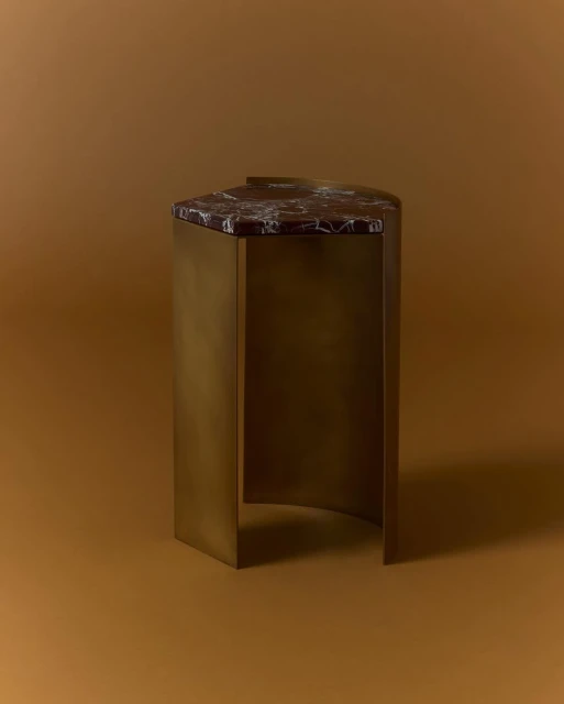 Side table with a geometric top made of dark marble and bronze metal base against a tan backdrop in a studio environment.