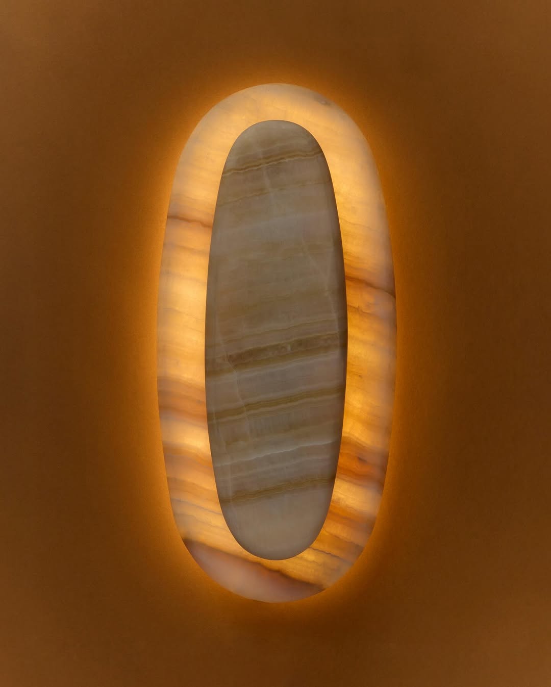 Abstract illuminated wall decor with a central marble section and a border of glowing warm light, casting soft light against the plain wall.