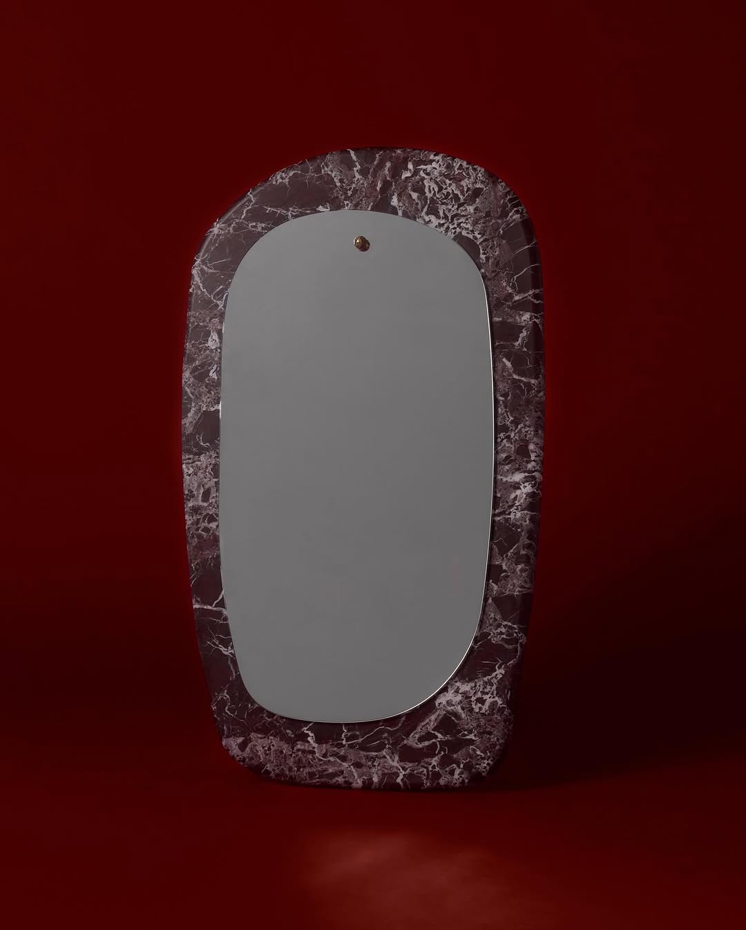 Rectangular mirror with rounded edges, set in a marble-patterned frame against a deep red background, featuring a modern, minimalist design.