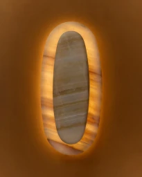 Close-up of an oval translucent stone wall sconce emitting a warm backlit glow against a warm beige textured wall.