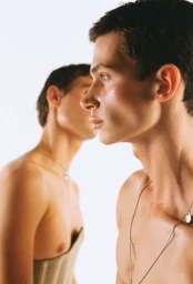 Profile portrait of two shirtless young men wearing silver necklaces against a bright white background for Fucking Young