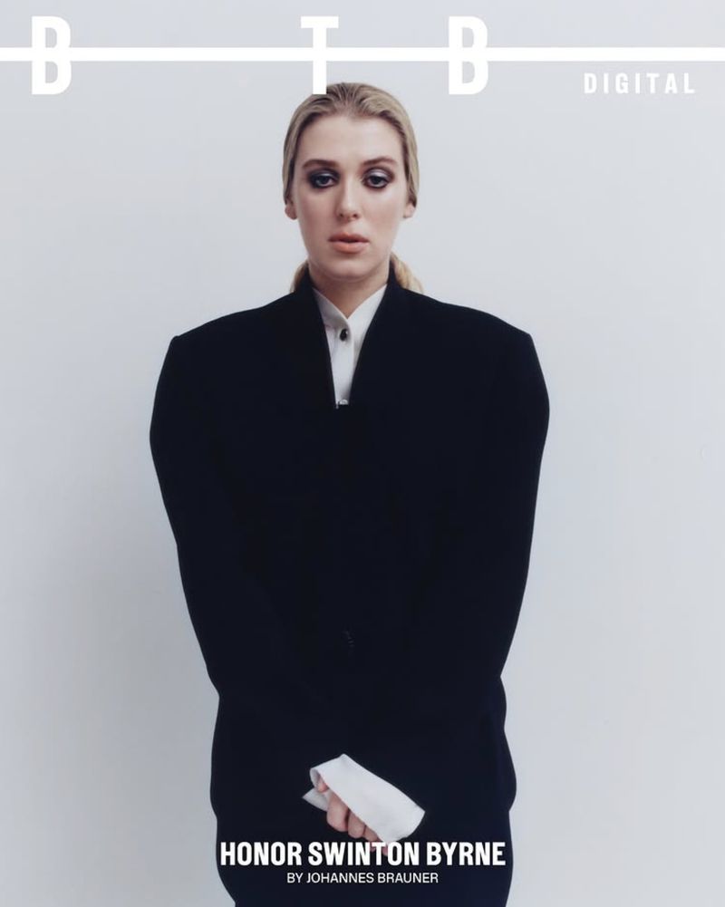 A magazine cover features Honor Swinton Byrne in a dark blazer and collared shirt against a bright white backdrop with bold sans-serif typography.
