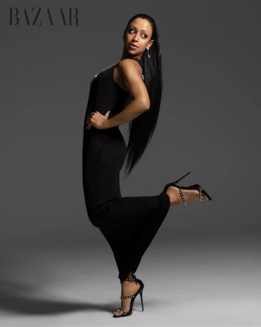 Liza Koshy posing in a long black dress and high heels against a neutral grey studio backdrop