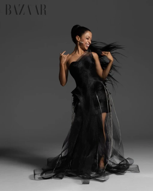 Liza Koshy wearing a black tulle gown with dynamic hair against a neutral grey background for Harper's Bazaar Vietnam editorial.