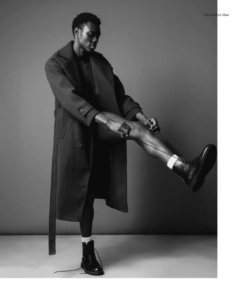 Black and white portrait of a Black male fashion model tying the laces of a pair of high-laced leather boots in a studio setting.