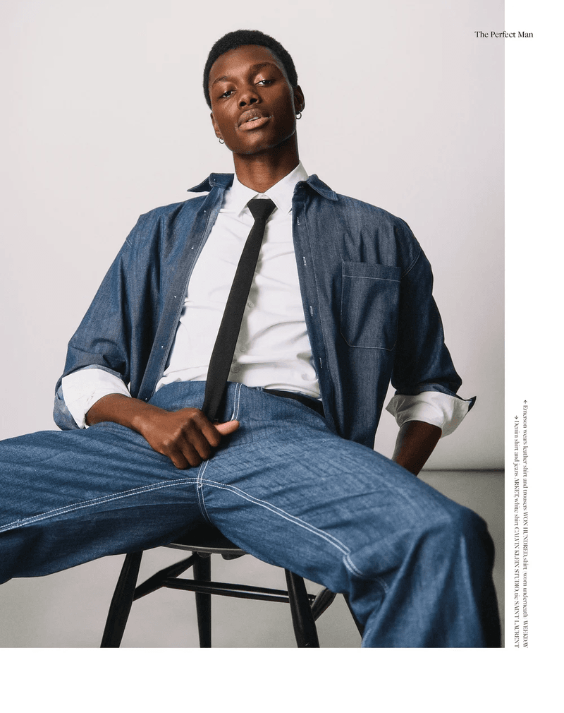 Model Emerson Pereira seated on a chair wearing a blue denim shirt, white dress shirt, black tie, and wide denim pants.