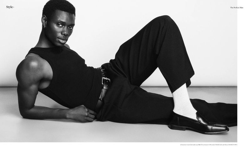Model Emerson Pereira reclining in a black tank top and trousers with white socks and loafers against a seamless backdrop.