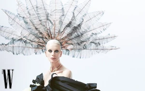 Model Kristen McMenamy wearing an elaborate feathered headpiece and black gown against a white background for W Korea.