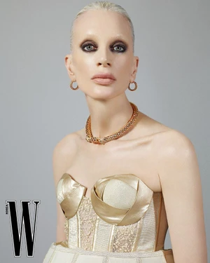 Model Kristen McMenamy in a gold structured top and necklace against a grey backdrop for W Korea