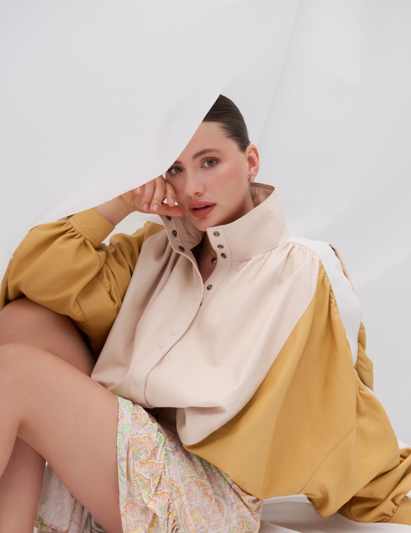 Woman in cream and mustard-yellow blouse sitting against white background. Fashion shot of a woman wearing designer shirt and skirt.