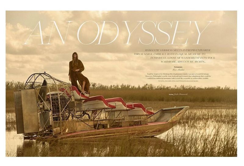 Woman in a jumpsuit poses on an airboat in a marsh landscape under an overcast sky, fashion editorial photography, Visie.