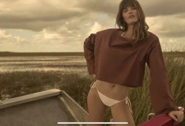 Model Ava Smith wearing brown long-sleeve crop top and bikini bottoms standing on a boat outdoors for Red Magazine.