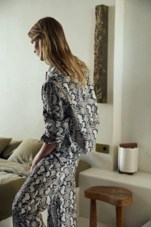 Adult female with blonde hair wearing a snake print pajama set indoors in a naturally lit setting. Fashion and lifestyle content.