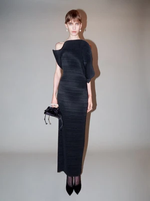 Model in a black sculptural dress holding a dark handbag against a plain neutral backdrop for Magda Butrym F/W 2025.