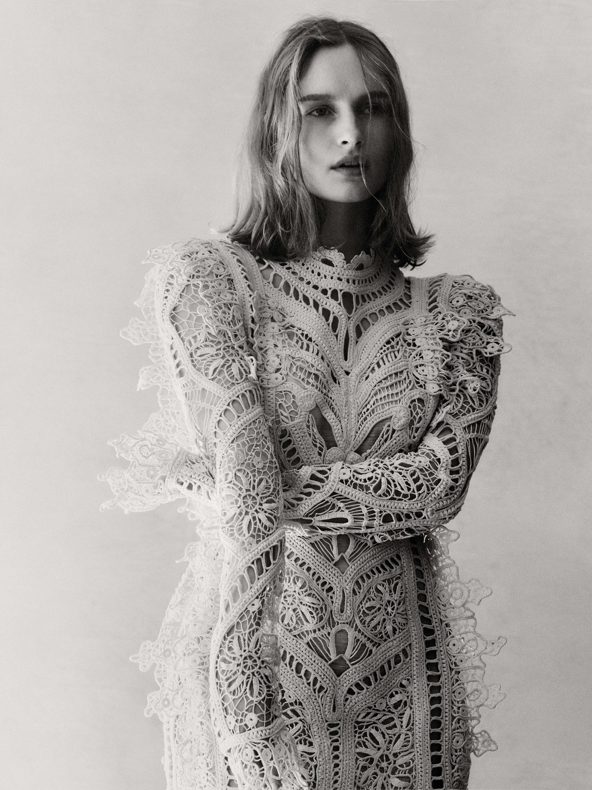 Portrait of an adult woman in a lacy white dress, posing in front of a neutral background, photographed in black and white.