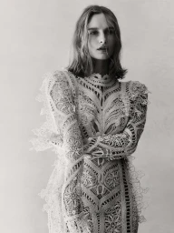 Olivia De Jonge wearing an intricate white lace long sleeve dress against a plain studio background in a portrait photograph by Georges Antoni.