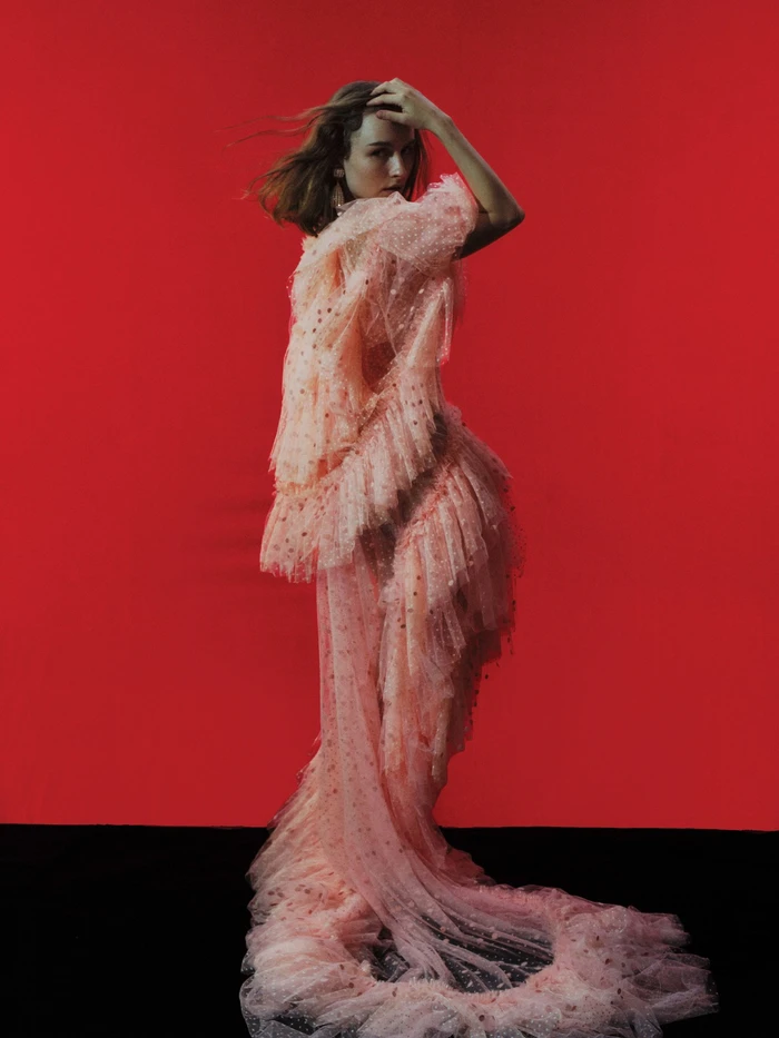 Olivia De Jonge wearing a pink ruffled tulle gown against a red backdrop for T Magazine, photographed by Georges Antoni.