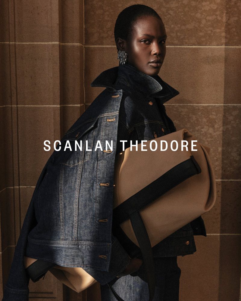 Elegant Black woman in a denim jacket carrying a tote bag against a neutral background, showcasing modern fashion and sophisticated style.