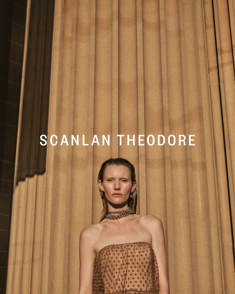 Fashion portrait of a blonde adult female wearing a brown strapless top with a beaded choker necklace in front of fluted columns.