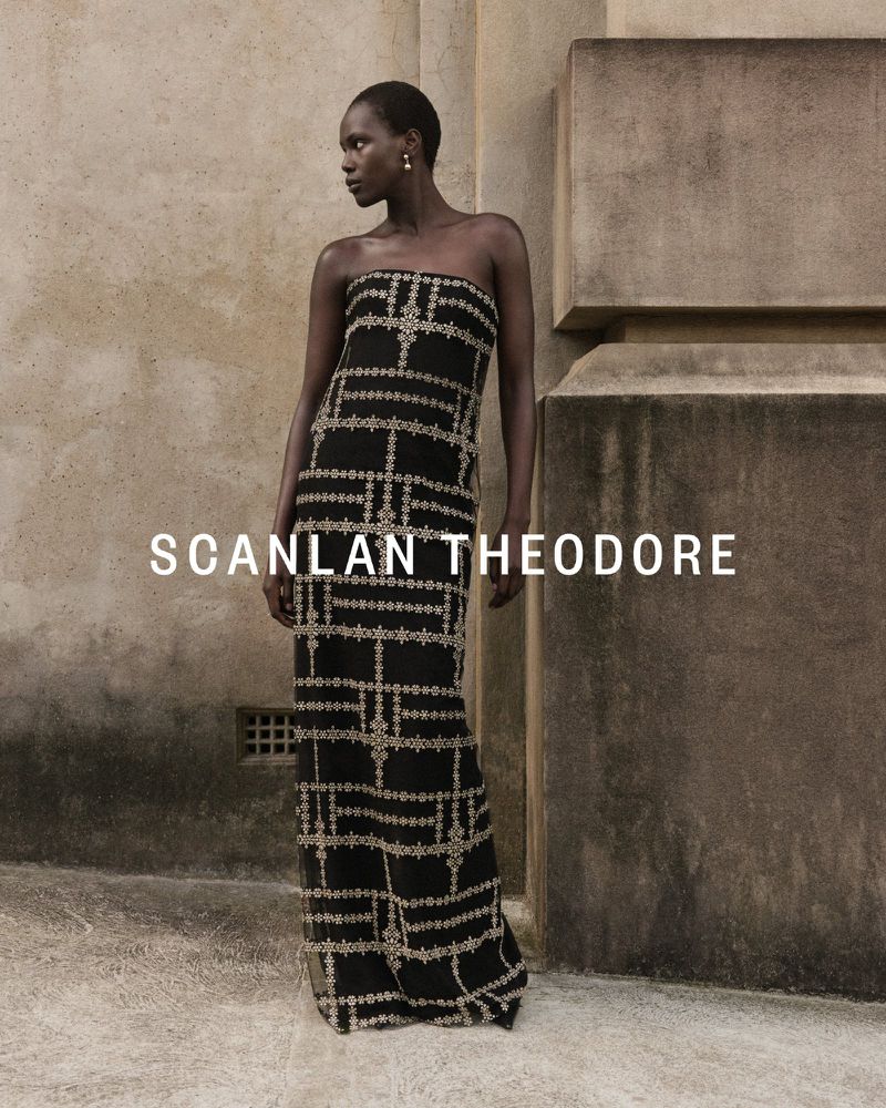 Model Achok Akoi in a strapless black embroidered column gown standing beside a textured stone wall for Scanlan Theodore.